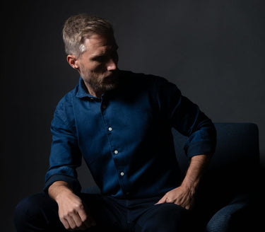 Man wearing a blue shirt sitting against a dark background