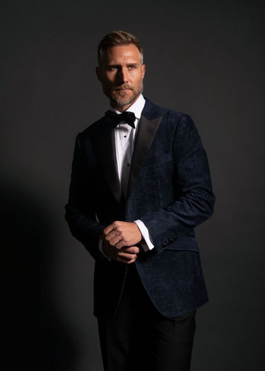 Man in a dark blue suit with a bow tie against a black background