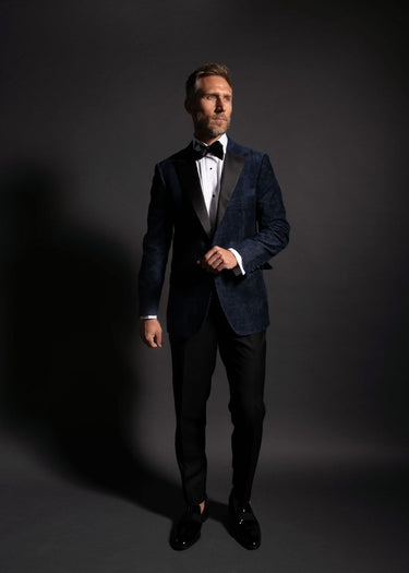Man wearing a black tuxedo with a bow tie on a dark background