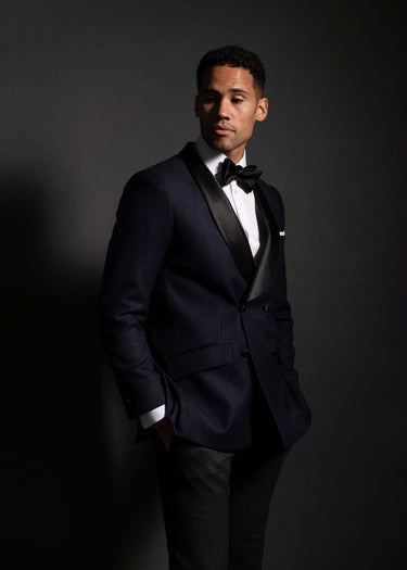 Man wearing a black tuxedo with a white shirt and black bow tie against a dark background