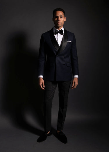 Man wearing a black tuxedo with a white shirt and black bow tie on a dark background