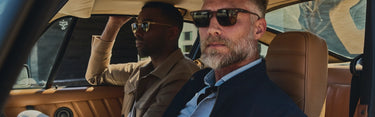 Two men in a car, one driving and the other sitting in the passenger seat, wearing sunglasses.