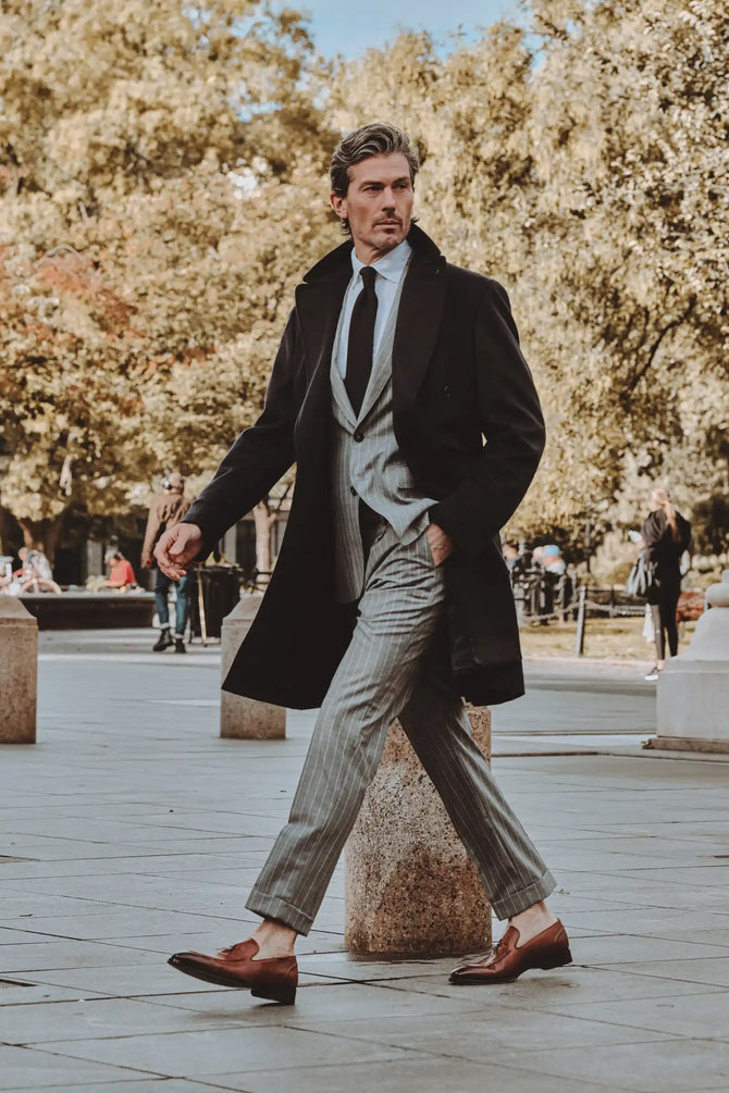 Man in a formal outfit walking outdoors with trees in the background