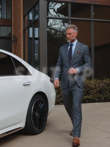 Man in a suit walking towards a white car outside a building